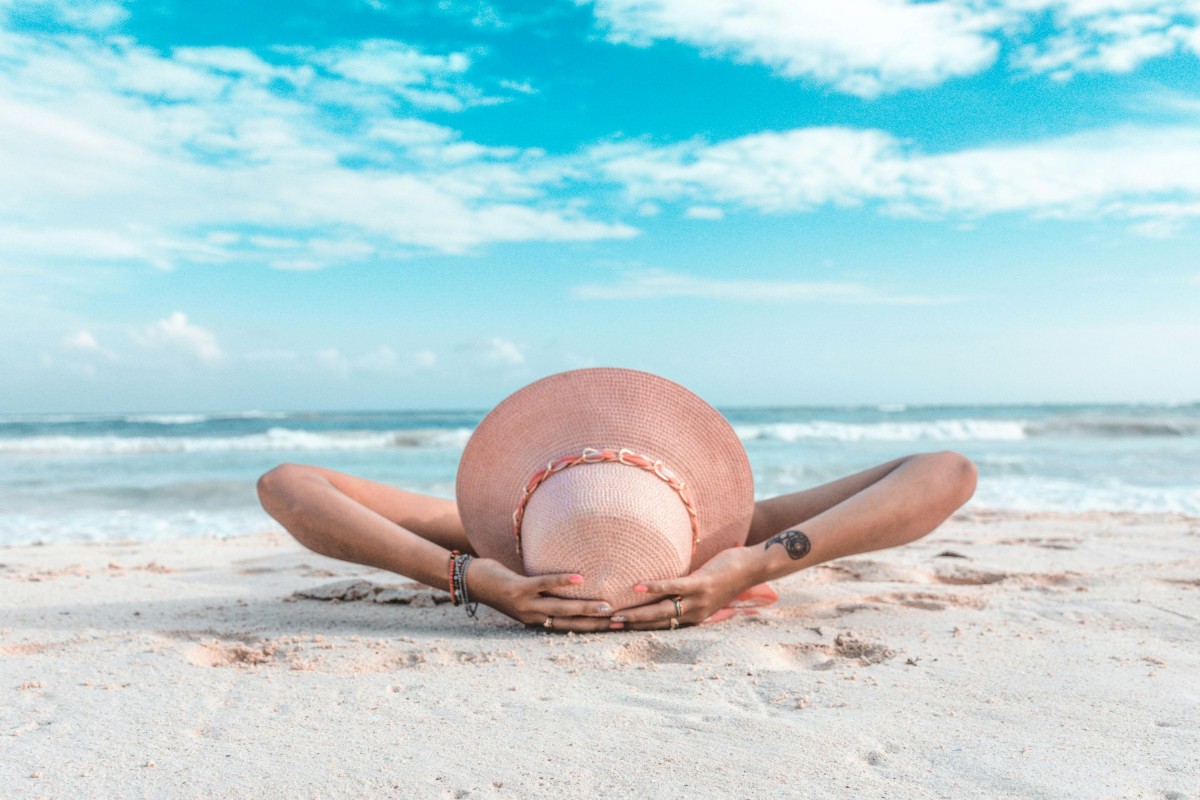 Zdjęcie kobiety w słomkowym kapeluszu leżącej na piaszczystej plaży nad morzem